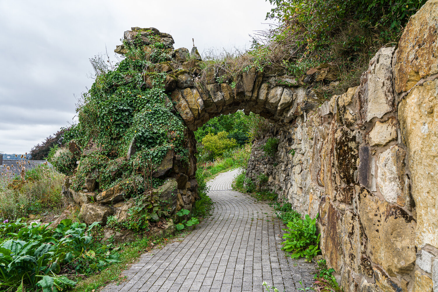 Ein gepflasterter Weg führt durch einen alten, grob gemauerten Torbogen hindurch